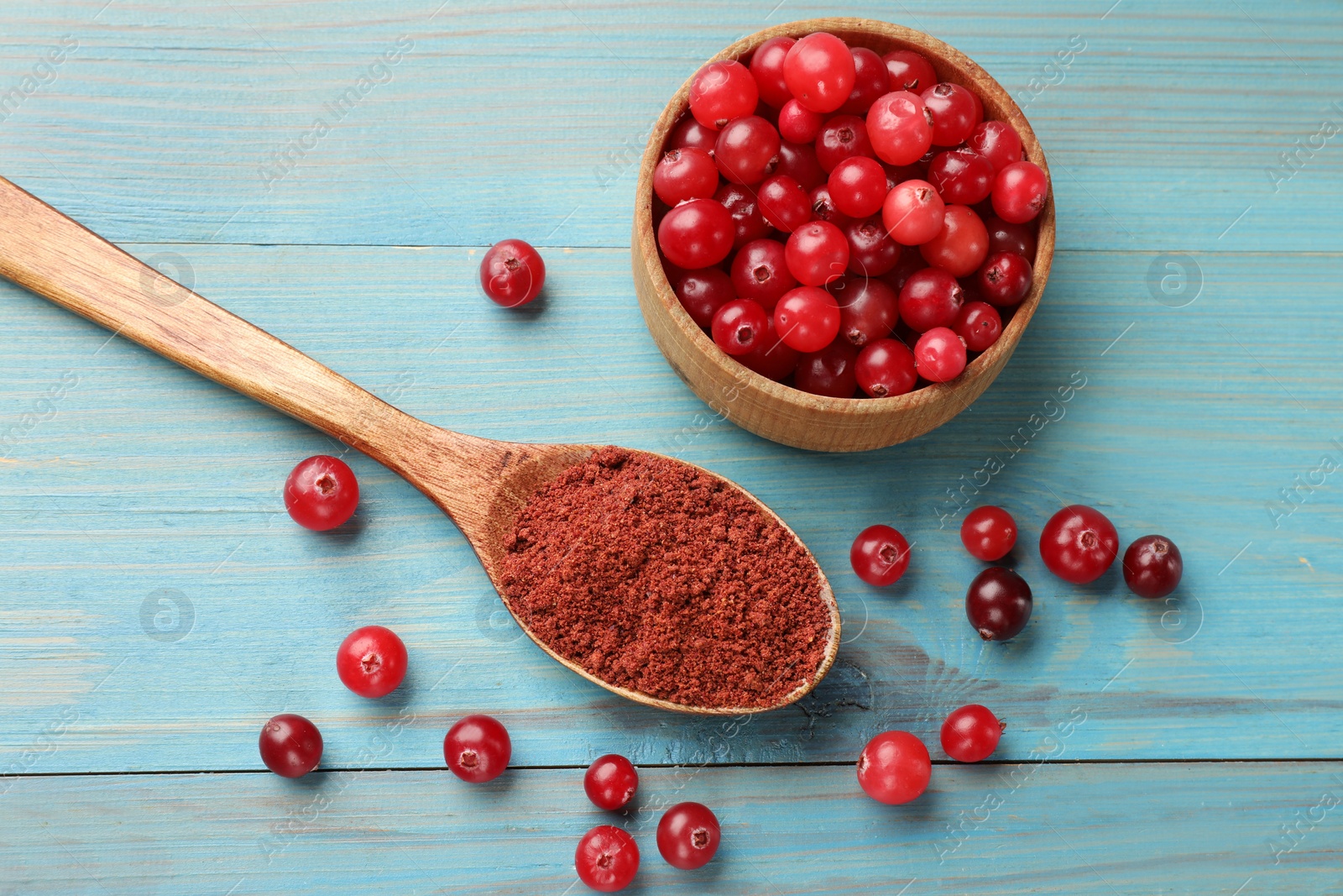 Photo of Spoon with cranberry powder and fresh berries on light blue wooden table, flat lay