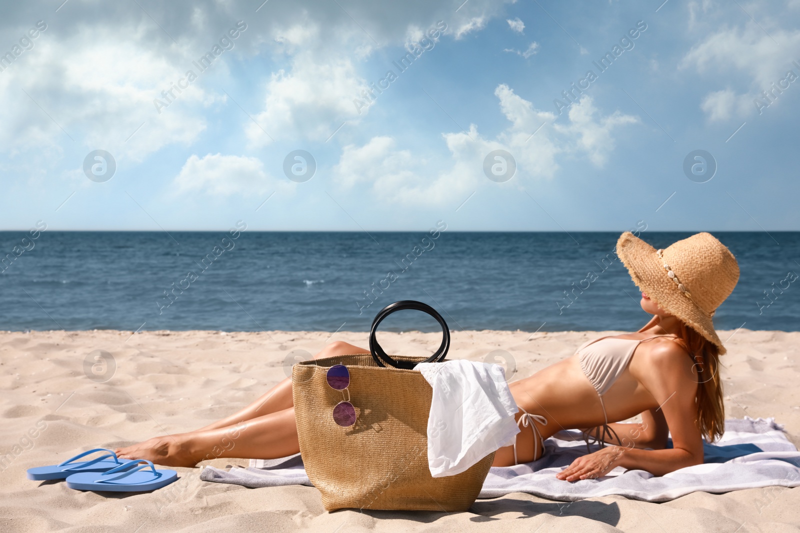 Photo of Woman with beach bag and straw hat on sand near sea