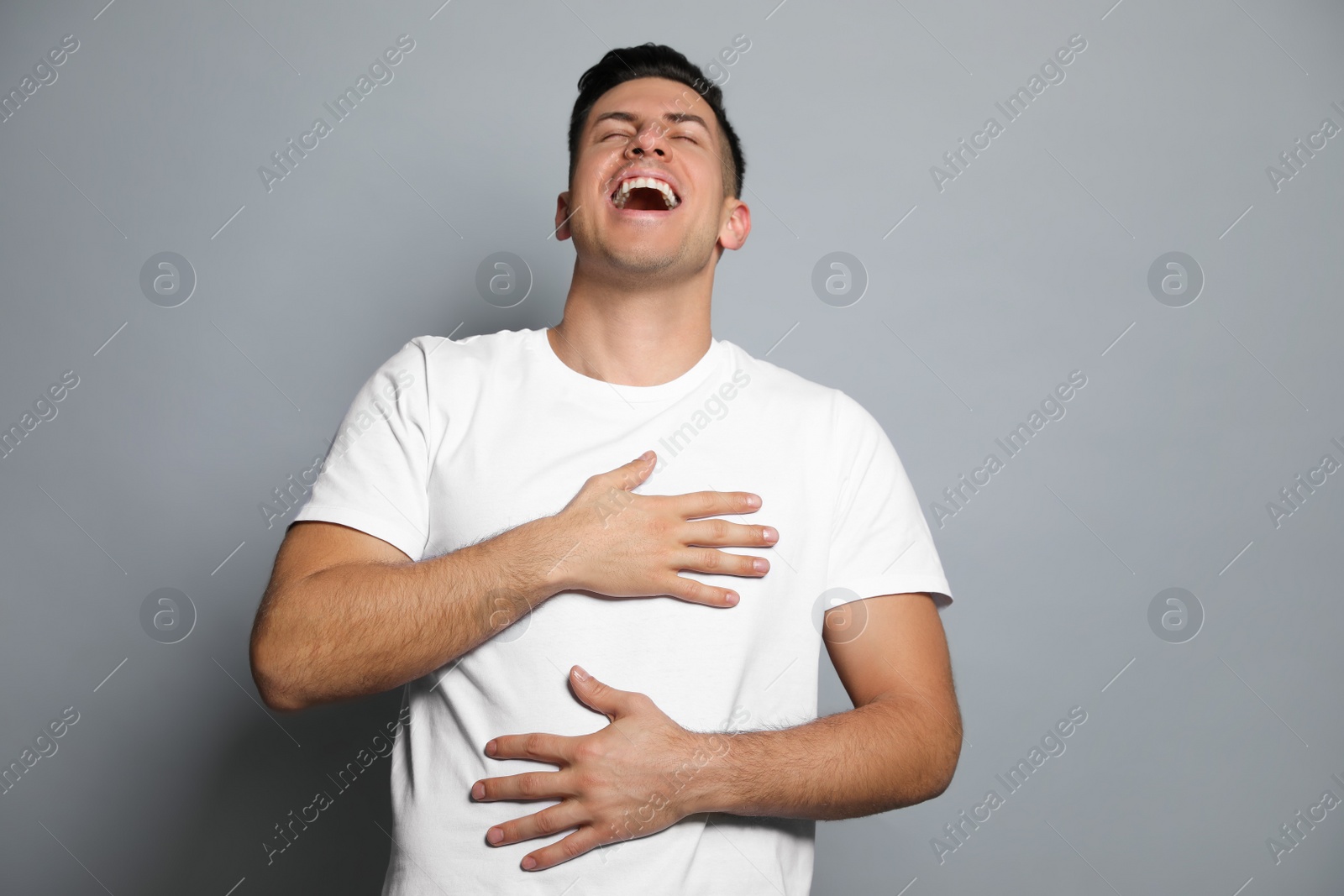 Photo of Handsome man laughing on grey background. Funny joke