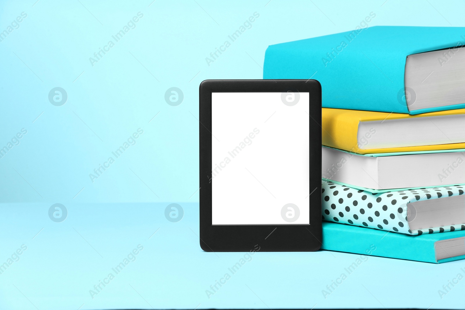 Photo of Modern e-book reader and stack of hard cover books on light blue background. Space for text