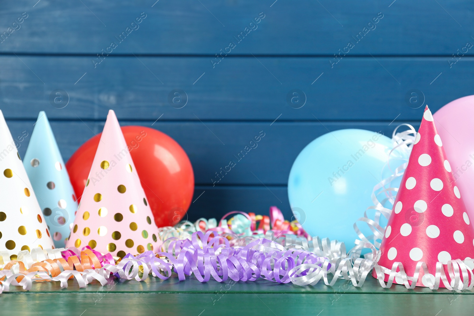 Photo of Colorful serpentine streamers, balloons and party hats on green wooden table. Space for text