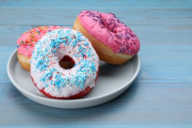 Photo of Sweet glazed donuts decorated with sprinkles on light blue wooden table, space for text. Tasty confectionery