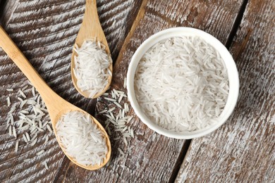 Photo of Raw basmati rice in bowl and spoons on wooden table, flat lay