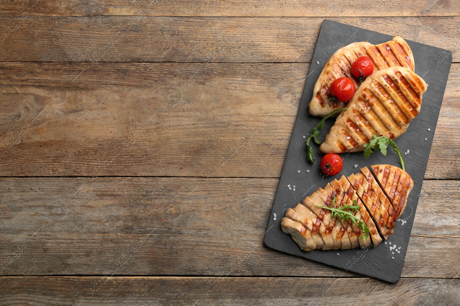 Photo of Tasty grilled chicken fillets with tomatoes and arugula on wooden table, top view. Space for text