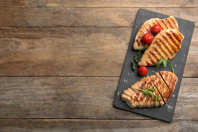 Tasty grilled chicken fillets with tomatoes and arugula on wooden table, top view. Space for text