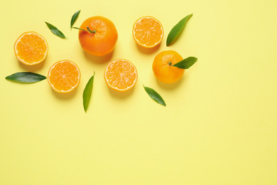 Flat lay composition with fresh ripe tangerines and leaves on light yellow background, space for text. Citrus fruit