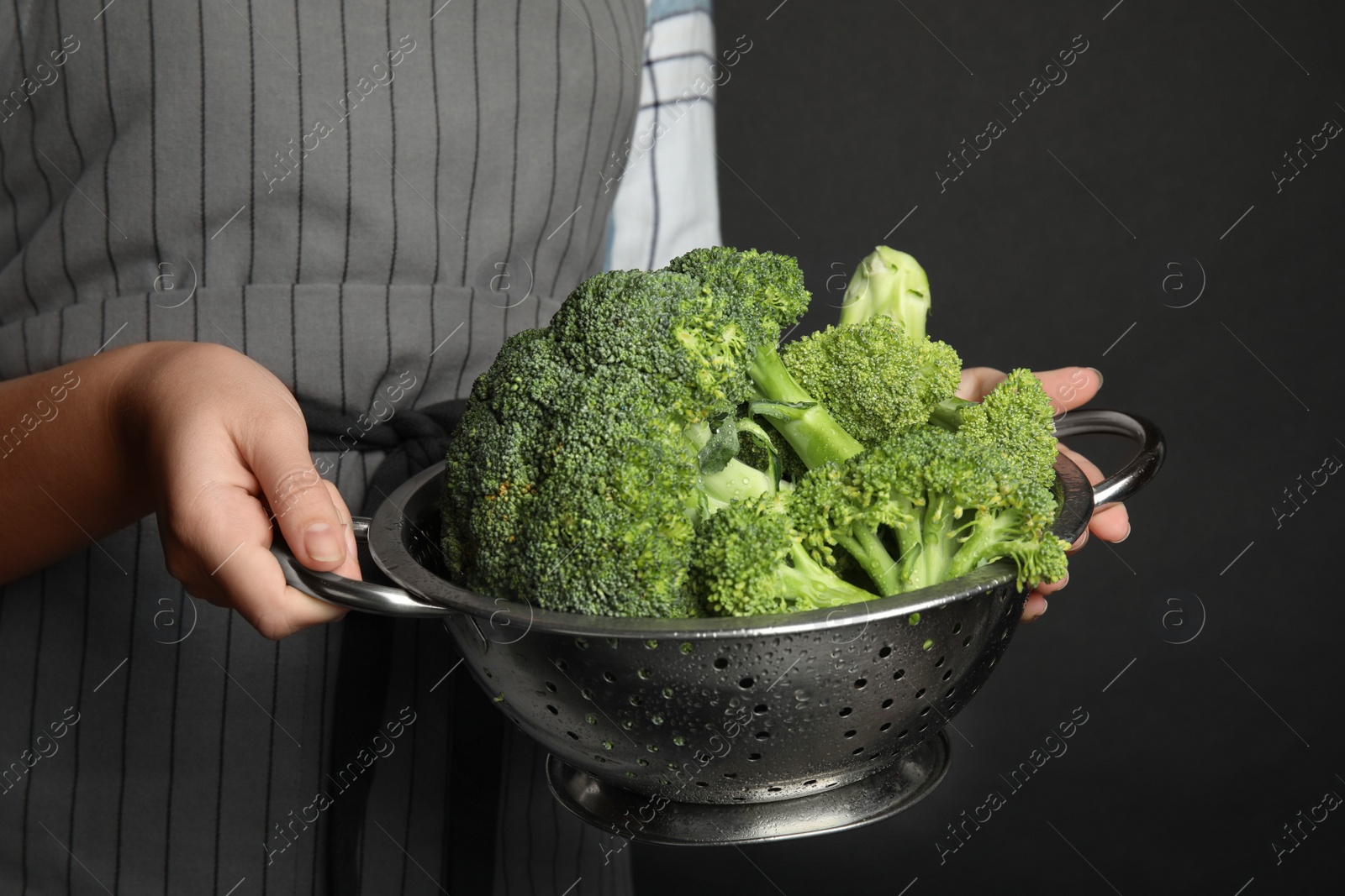 Photo of Woman holding colander with fresh green broccoli on black background, closeup