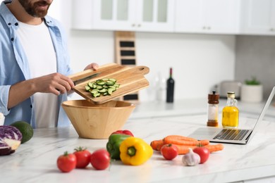 Photo of Man making dinner while watching online cooking course via laptop in kitchen, closeup