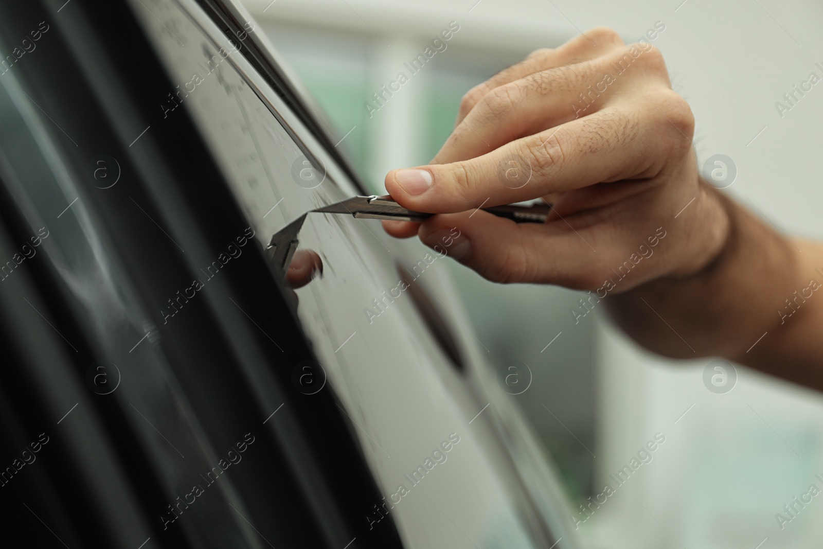 Photo of Worker tinting car window with foil in workshop, closeup