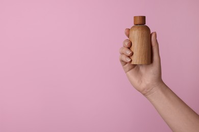 Woman holding bottle of cosmetic product on pink background, closeup. Space for text