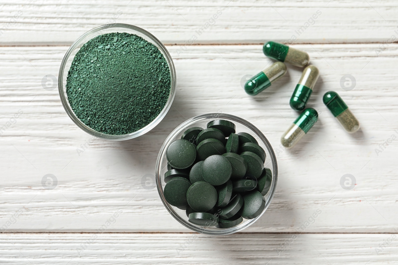 Photo of Bowls of spirulina pills and powder on wooden background, top view