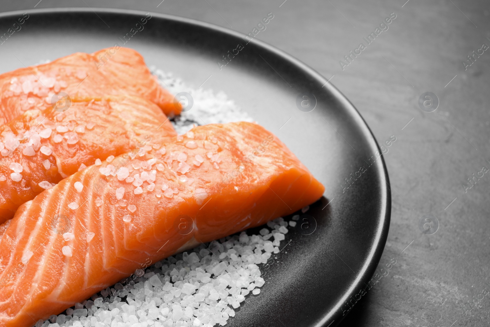 Photo of Fresh raw salmon with salt on black table, closeup. Space for text