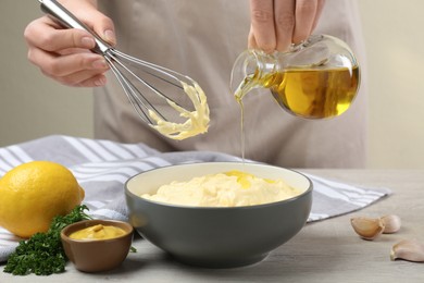 Photo of Woman making homemade mayonnaise in ceramic bowl at wooden table, closeup