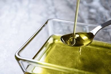 Pouring hemp oil into spoon over glass bowl, closeup