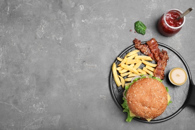 Photo of Frying pan with tasty hamburger and french fries on grey background, top view. Space for text