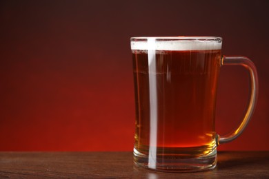 Photo of Mug with fresh beer on wooden table against color background, closeup. Space for text