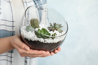 Woman holding florarium with different succulents on color background, closeup. Space for text
