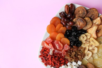 Plate with different dried fruits on violet background, top view. Space for text