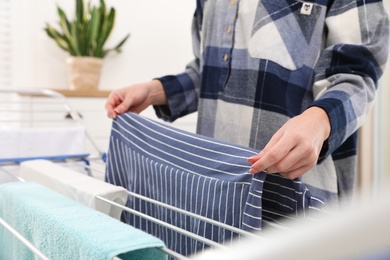 Photo of Young woman hanging clean laundry on drying rack at home, closeup