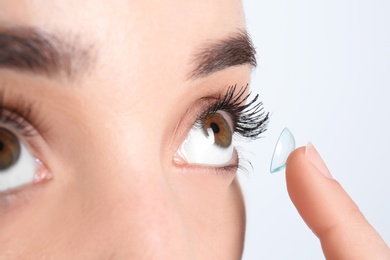 Photo of Young woman putting contact lens in her eye, closeup