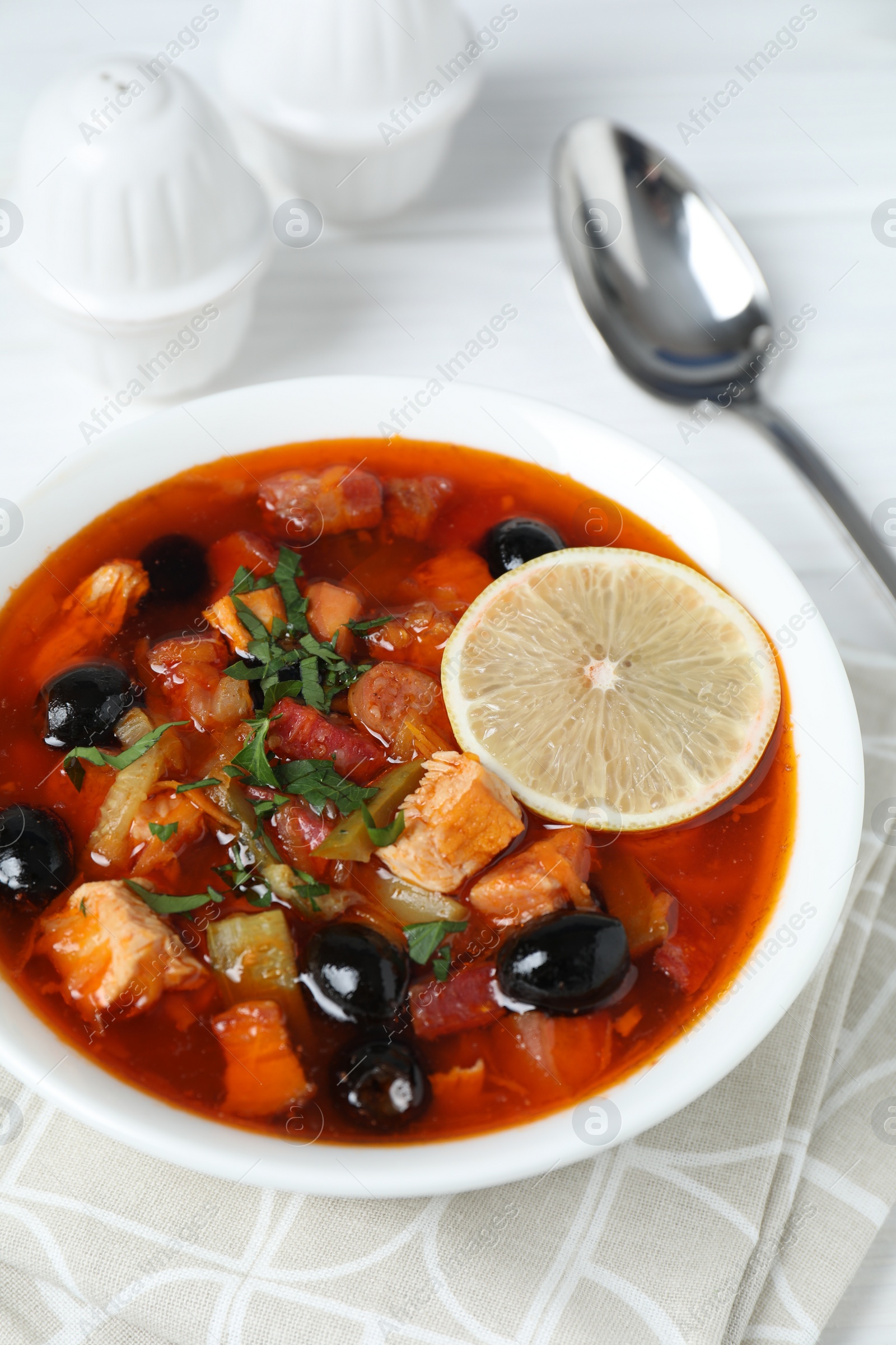 Photo of Meat solyanka soup with sausages, olives, vegetables and spoon on white table