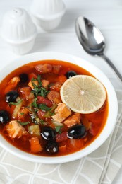 Meat solyanka soup with sausages, olives, vegetables and spoon on white table