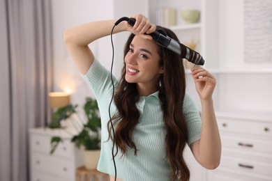 Photo of Smiling woman using curling hair iron at home