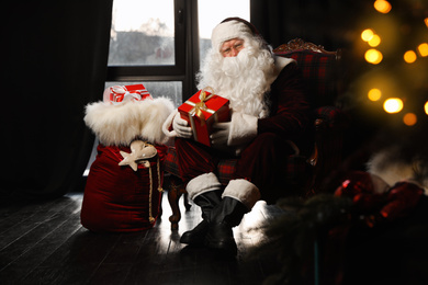 Photo of Santa Claus with Christmas gifts in armchair near window indoors