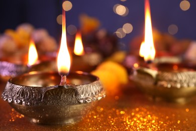 Photo of Diwali celebration. Diya lamp on shiny golden table against blurred lights, closeup and space for text