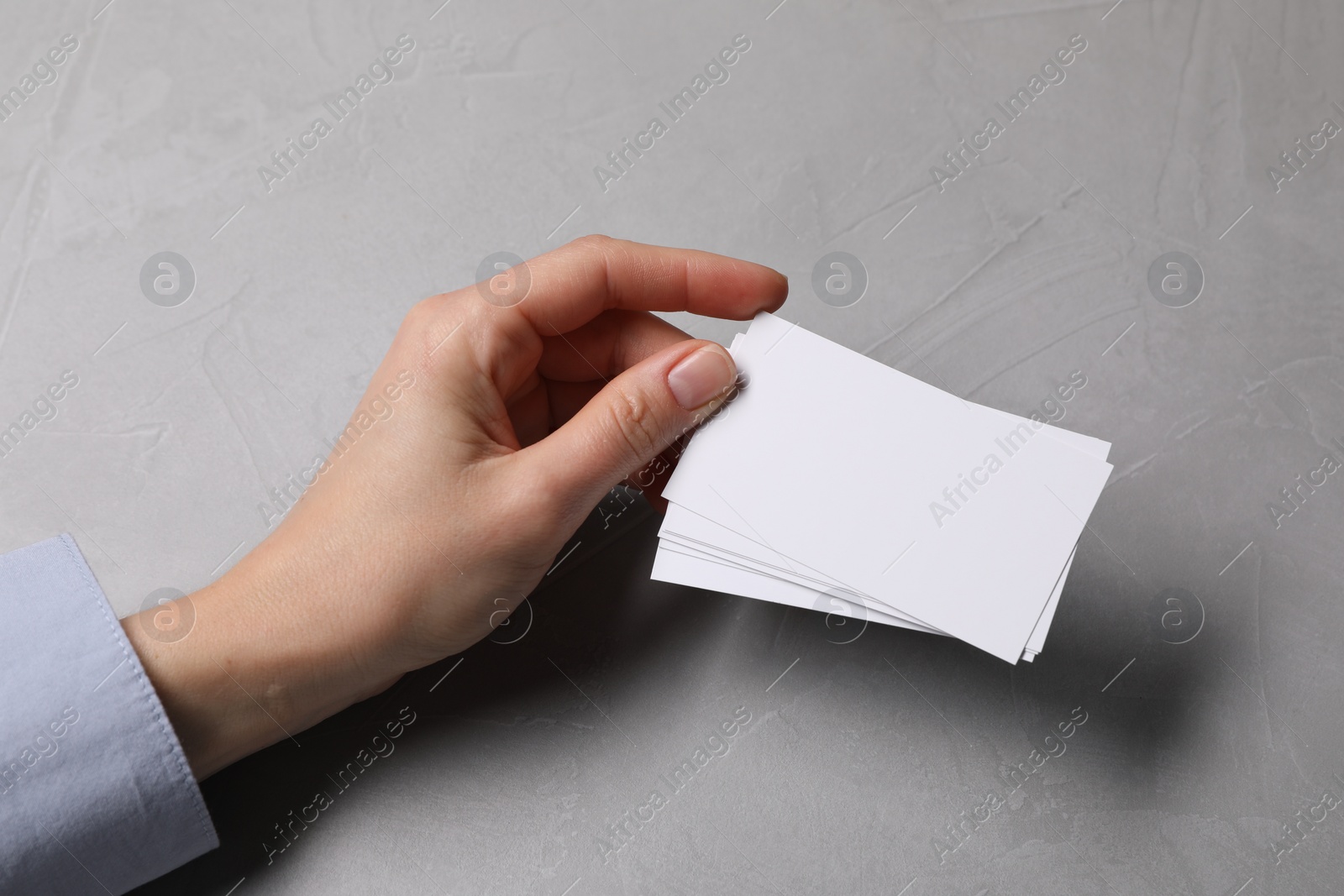 Photo of Woman holding blank cards at light grey table, closeup. Mockup for design