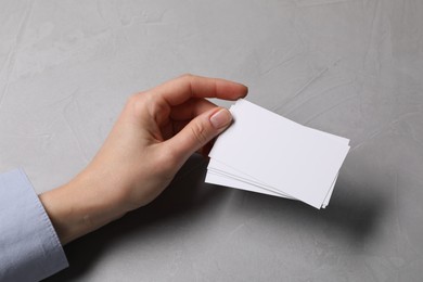 Photo of Woman holding blank cards at light grey table, closeup. Mockup for design