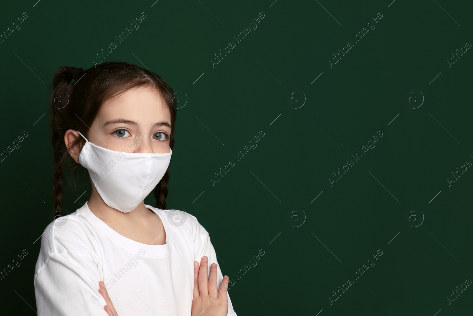 Photo of Girl wearing protective mask on green background, space for text. Child's safety from virus