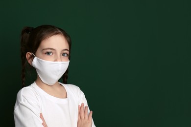 Photo of Girl wearing protective mask on green background, space for text. Child's safety from virus