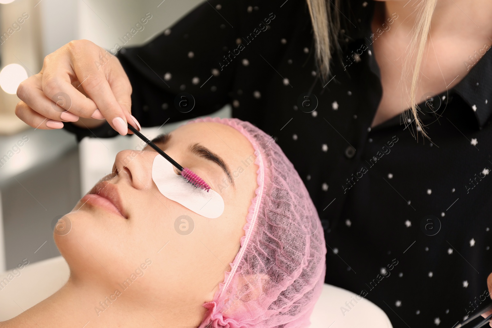 Photo of Young woman undergoing eyelash extensions procedure in salon