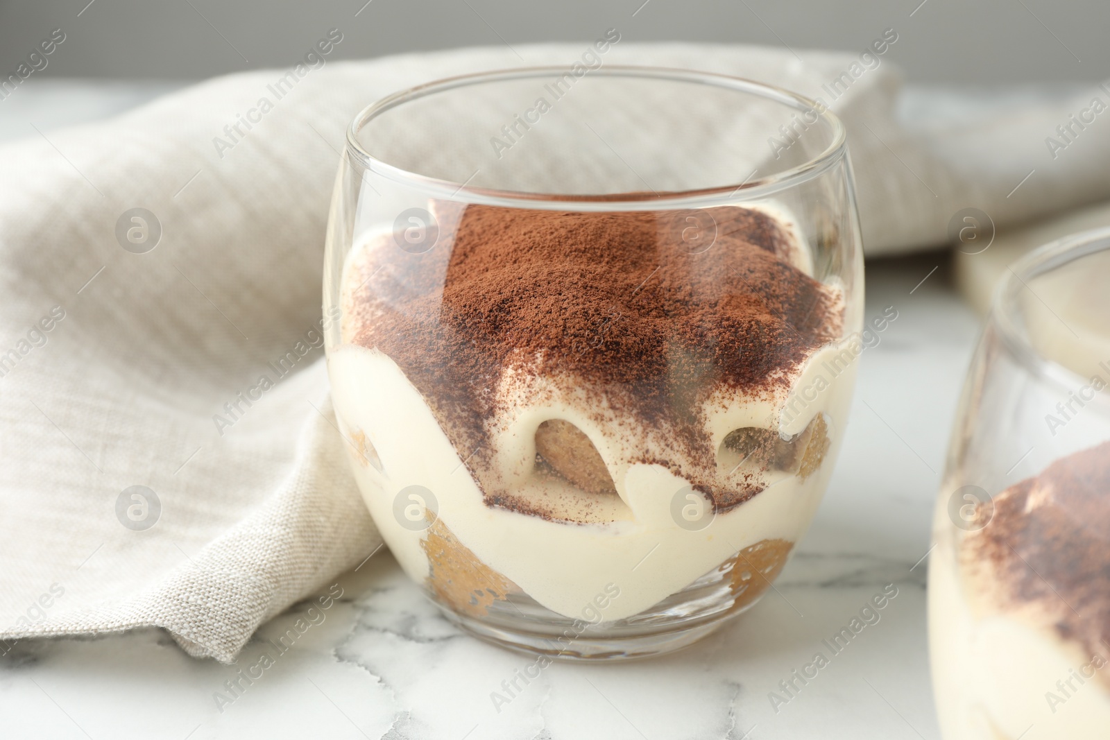 Photo of Delicious tiramisu in glasses on white marble table, closeup