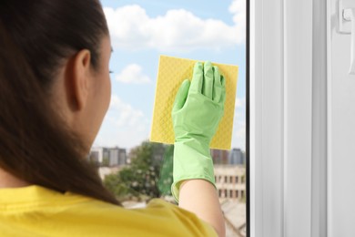 Photo of Woman cleaning window glass with sponge cloth indoors, closeup