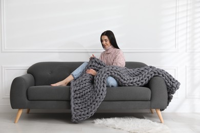 Photo of Young woman with chunky knit blanket on sofa at home