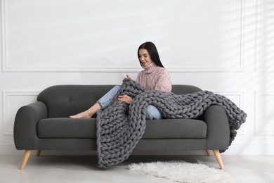 Young woman with chunky knit blanket on sofa at home