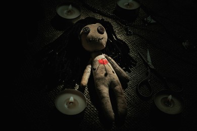 Image of Voodoo doll with pins surrounded by ceremonial items on burlap fabric