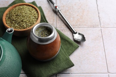 Photo of Calabash, bombilla, bowl of mate tea leaves and teapot on tiled table, space for text