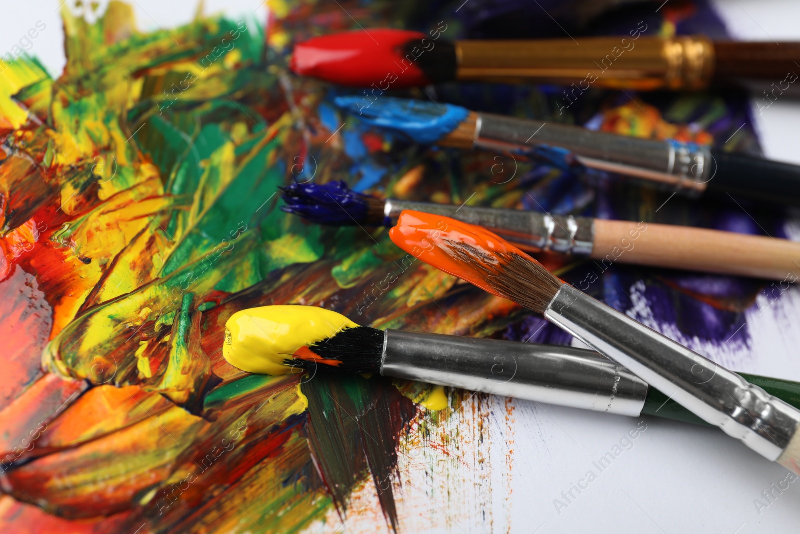 Photo of Set of brushes with different paints on artwork, closeup