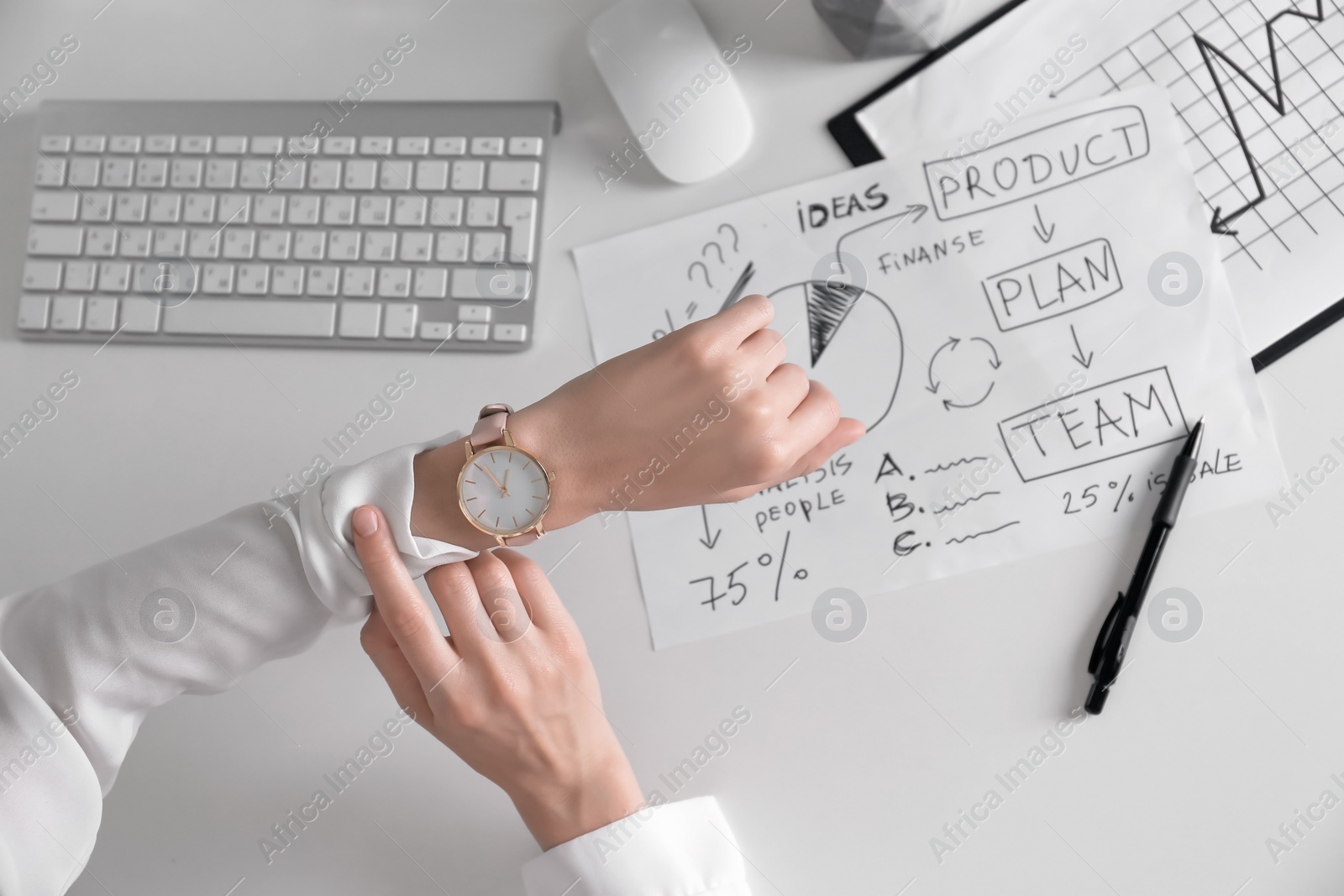 Photo of Young woman checking time on her wristwatch at workplace