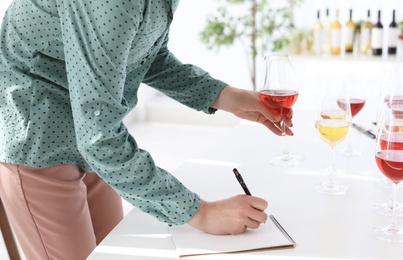 Woman with notebook tasting delicious wine at table indoors