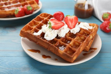 Photo of Delicious Belgian waffles with strawberries, whipped cream and caramel sauce on turquoise wooden table, closeup
