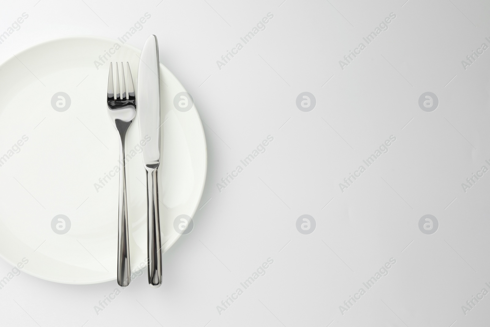 Photo of Plate, fork and knife on white background, top view. Space for text