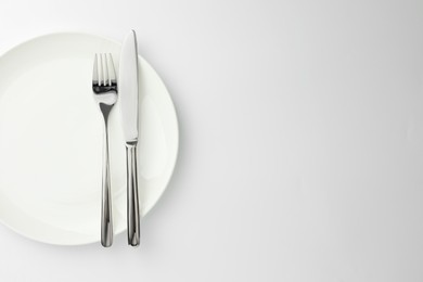 Photo of Plate, fork and knife on white background, top view. Space for text