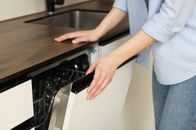 Photo of Woman opening dishwasher's door in kitchen, closeup