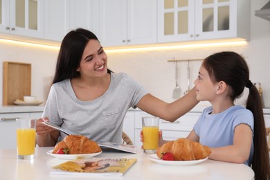 Photo of Happy mother and daughter having breakfast together in kitchen. Single parenting