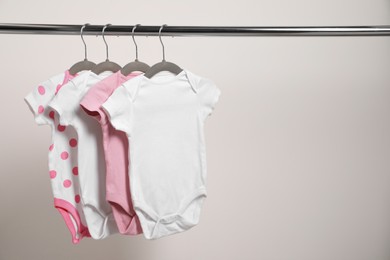 Photo of Baby bodysuits hanging on rack near white wall. Space for text