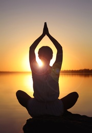 Photo of Woman practicing yoga near river on sunset. Healing concept